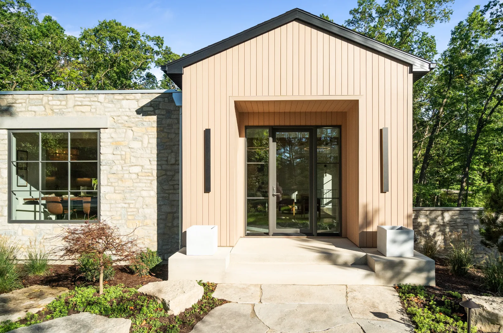 Entry, recessed under the gable between stone and vertical siding